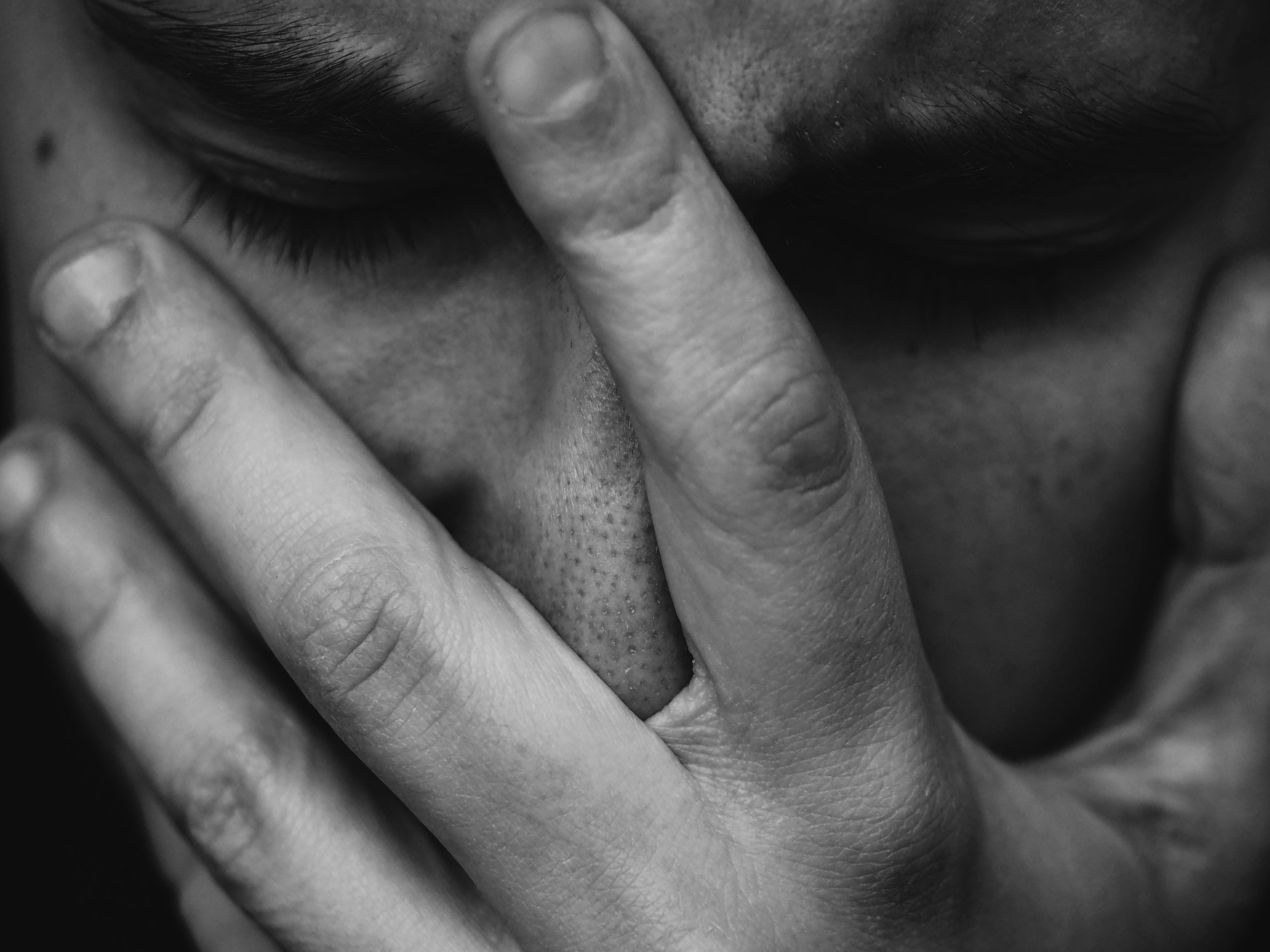 Imagem em preto e branco de um homem chorando com uma mão sob o rosto.